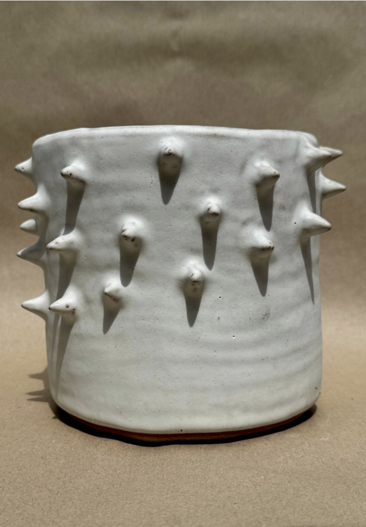 A cylindrical ceramic planter covered in hand-applied spikes